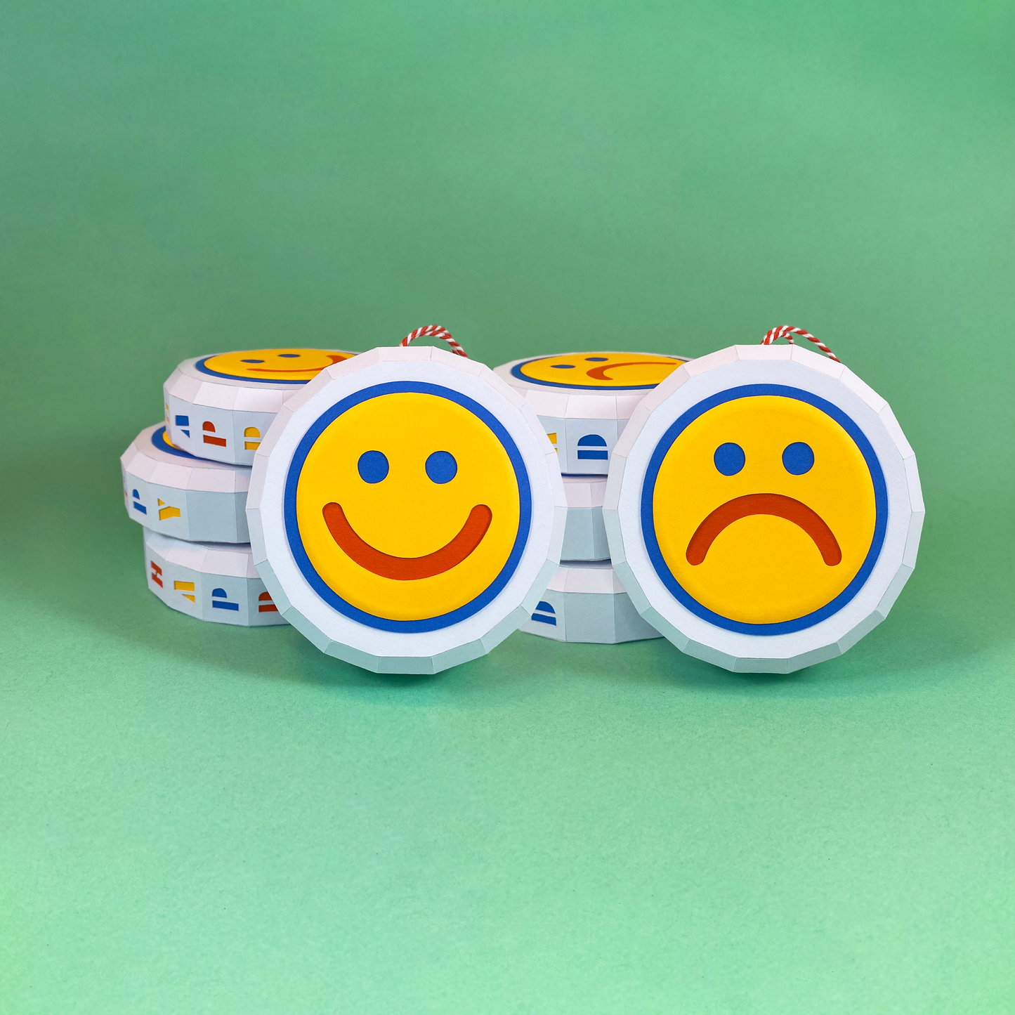 Two paper baubles with yellow faces. One is smiling the other is frowning.